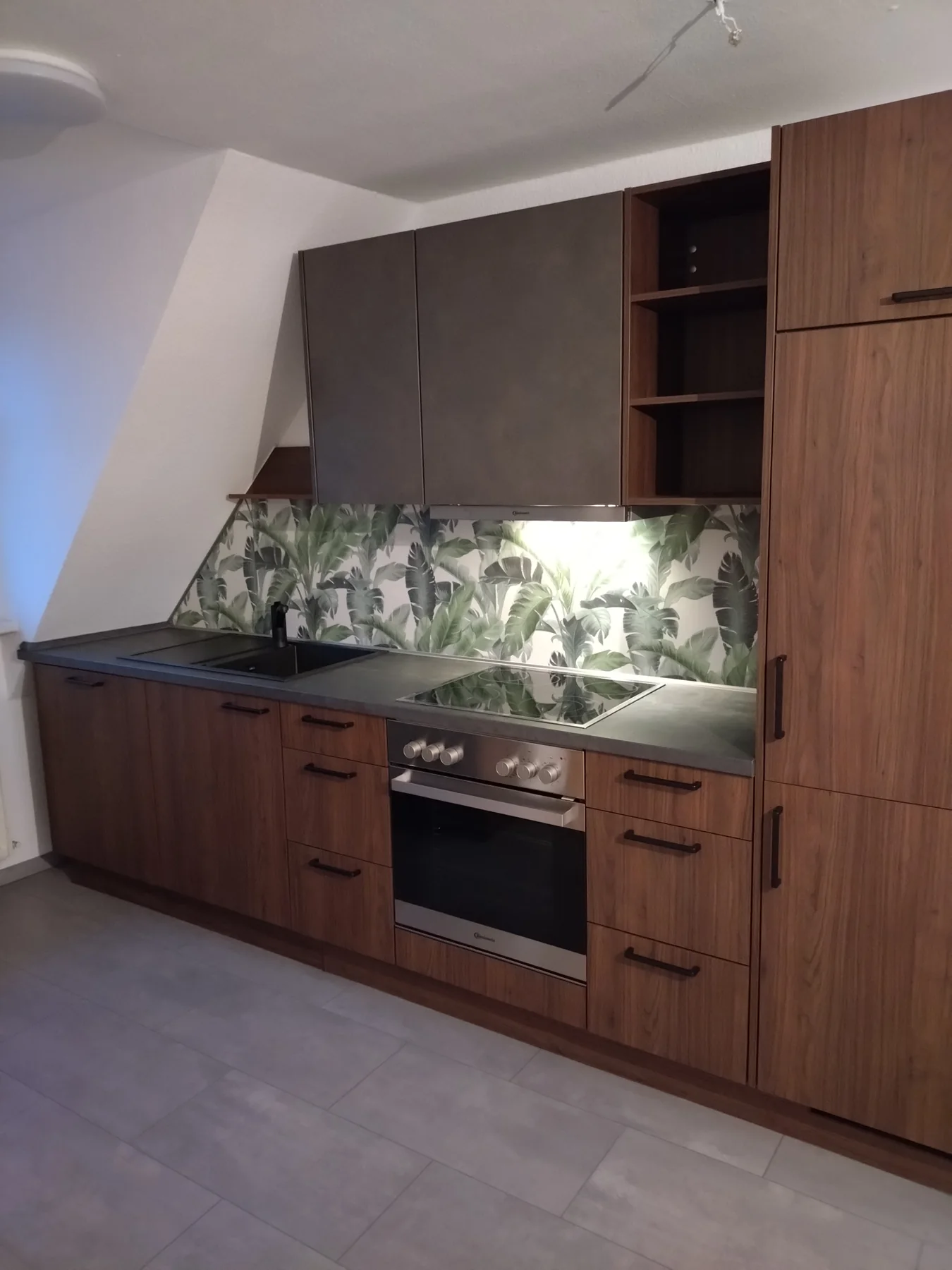 Passgenau montierte Küche unter einer Dachschräge mit Holzfronten und beleuchteter Pflanzenrückwand
