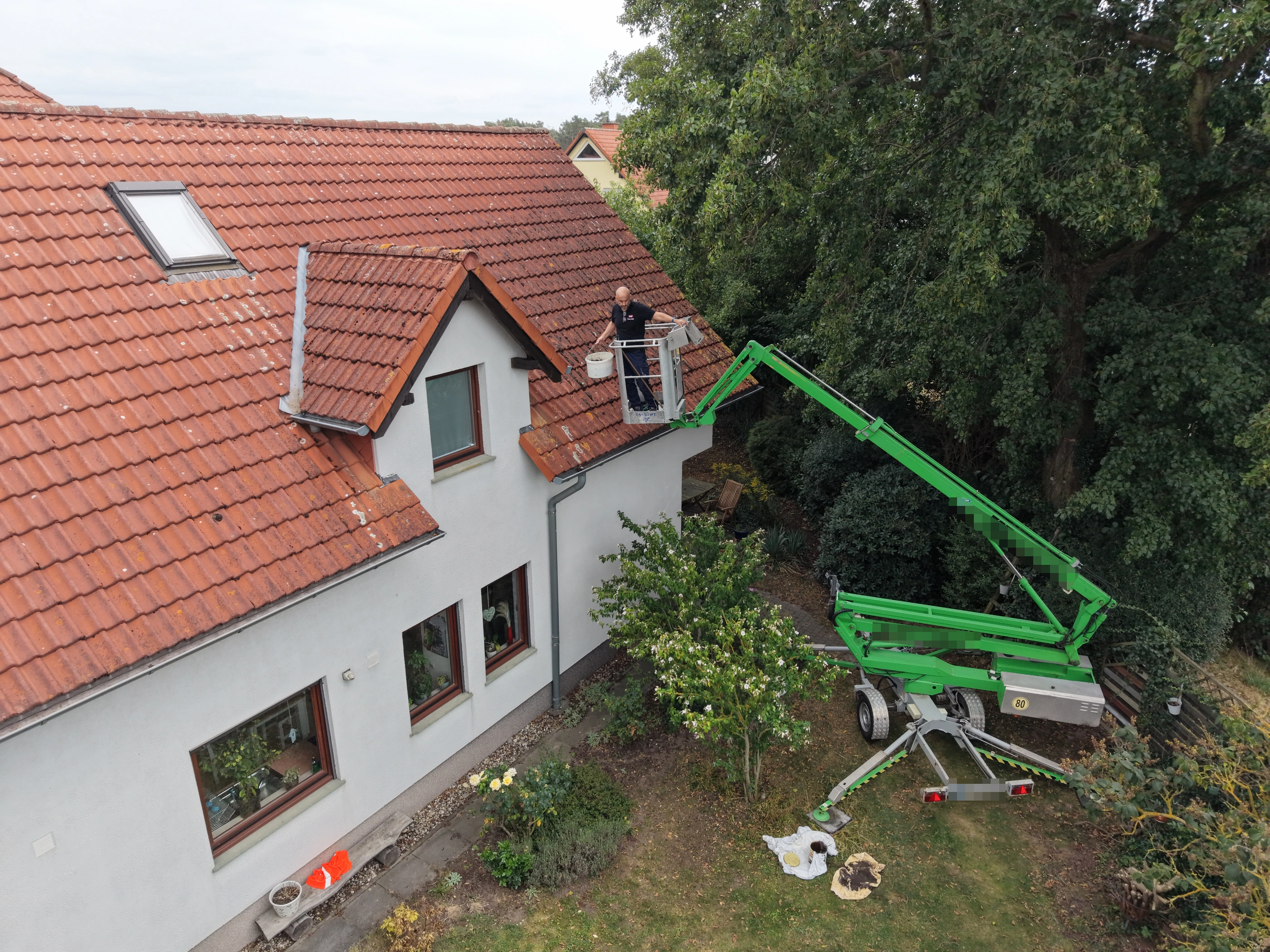 Arbeitsbühne mit ausgefahrenem Ausleger und abgestütztem Untergestell im Einsatz an der Dachrinne